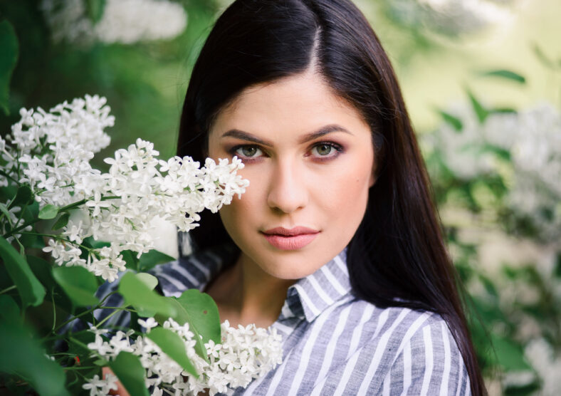 Portrait of a beautiful brunette whith a flowering tree. A young woman against the background of spring blooming apple trees. Natural makeup, outdoor portrait