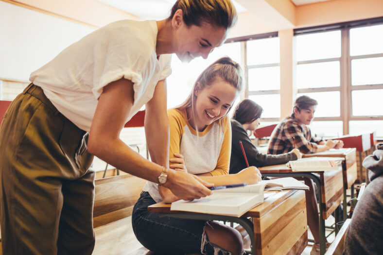 Happy female teacher assisting a teenage student in the classroom. Female professor helping girl student during a class at high school.