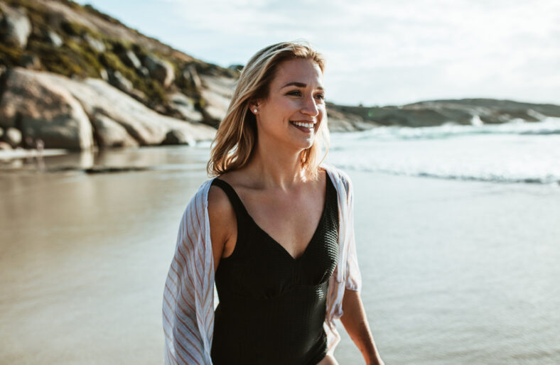 Woman walking along the sea shore. Female in swimwear walking on the beach.