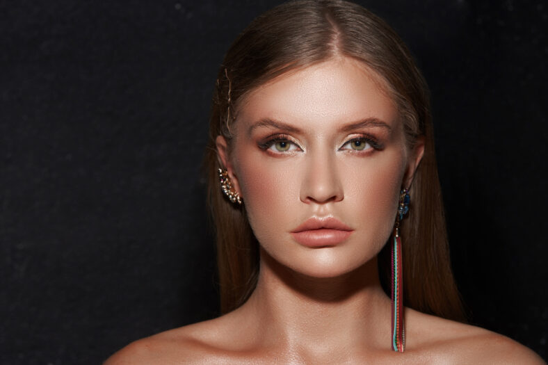 Beautiful fashion girl with stylish earrings and long dark straight hair. Coseup face portrait on black background.