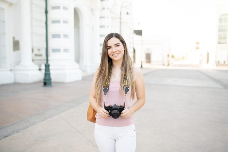Portrait of attractive Caucasian young woman with camera exploring city