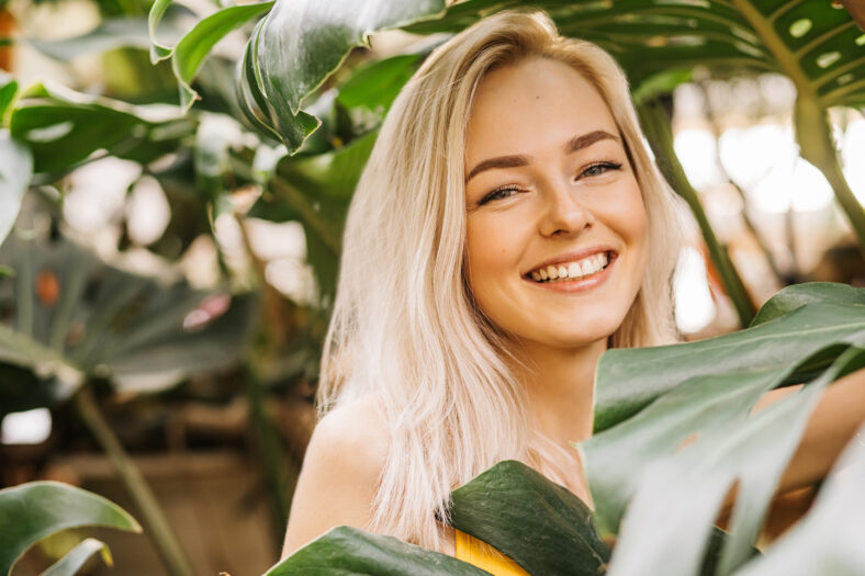 Portrait of gorgeous lady in stylish swimsuit posing in rainforest, enjoying summer, spending time in nature. Natural beauty concept. Blonde girl gentle smiling at camera.