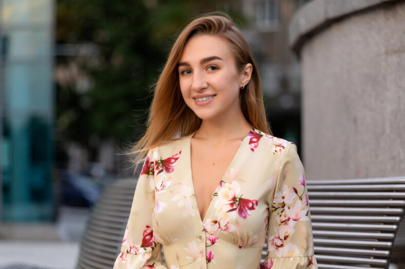Portrait of a beautiful young girl on a background of a blue business center dressed in a summer beige dress