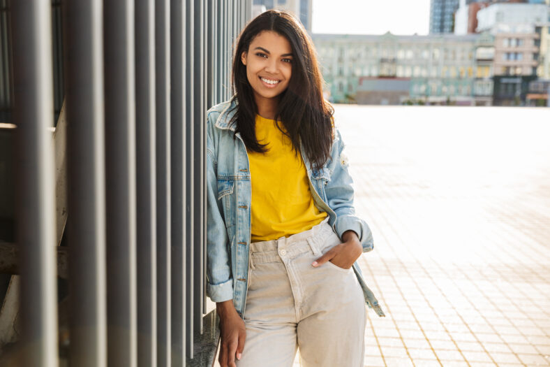 Image of joyful african american woman smiling and looking at camera while standing at city street