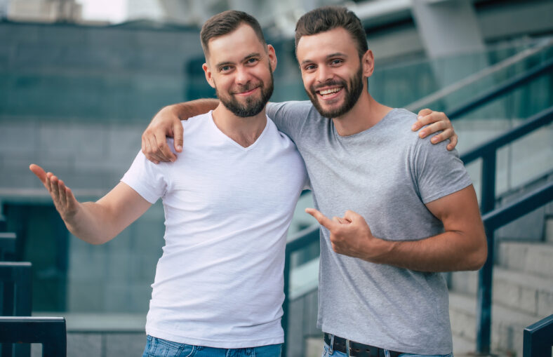 Two happy excited handsome bearded best friends in casual clothes are handshaking, hugging while standing outdoor.