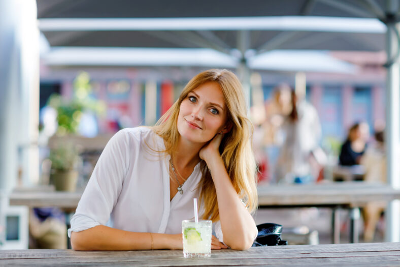 Mujer joven bebiendo cóctel de mojito en Cafe Terrace en el caluroso día de verano. Hermosa empresaria que disfruta de una noche cálida en el restaurante Afterwork. Feliz sonriente solo dama