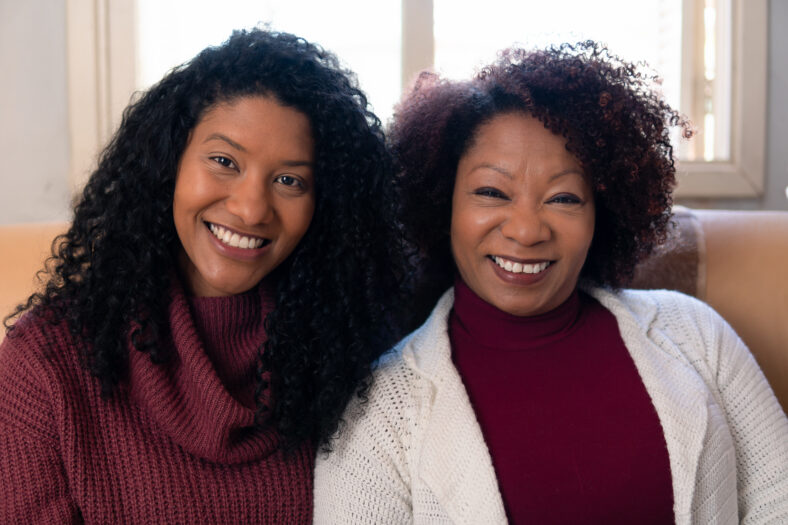 Portrait of brazilian adult daughter and mother sitting in couch looking at camera Inside the house in living room. Family, affectionate, reunion, together concept.