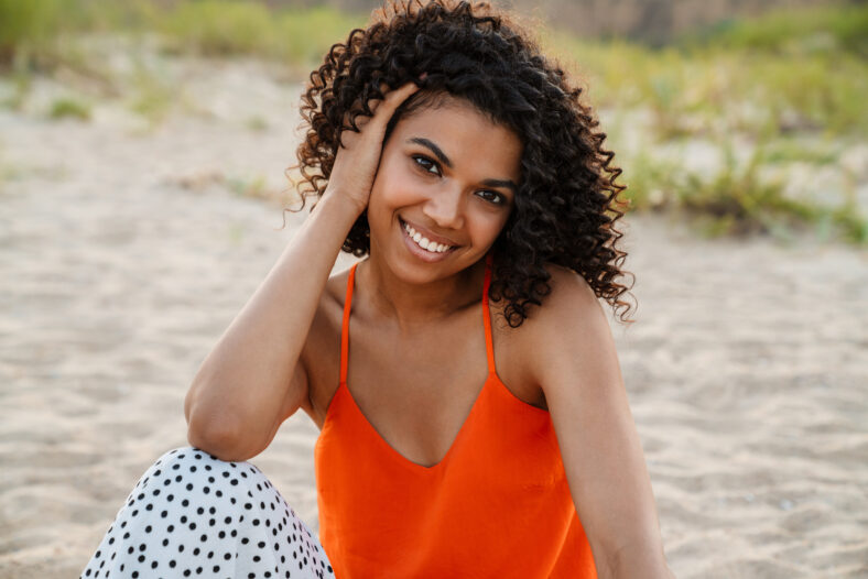 Image of beautiful happy young african woman walking at the beach outside
