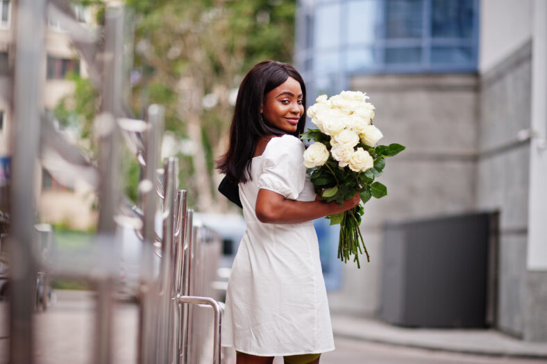 Beautiful african american girl holding bouquet of white roses flowers on dating in the city. Black businesswoman with bunch of flowers.