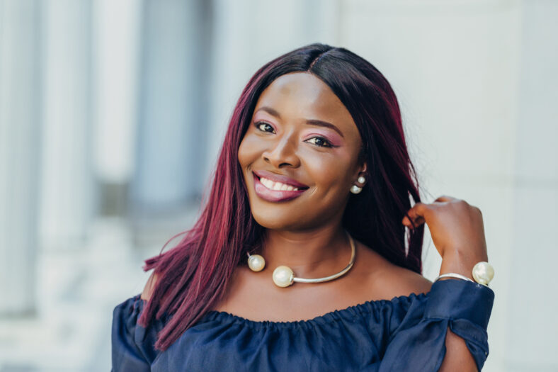 portrait of beautiful young african american woman in blue dress with pink hair hairstyle smiling and walking down the street