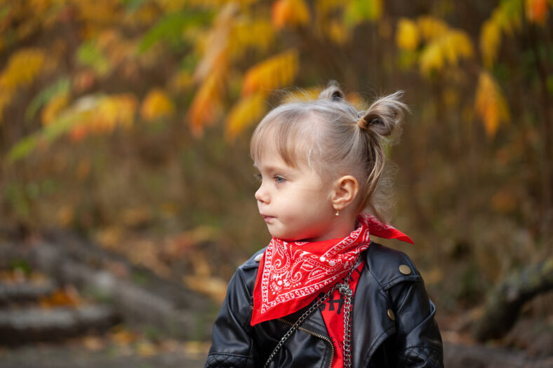 Closeup portrait of little girl turned head away from camera in autumn park.