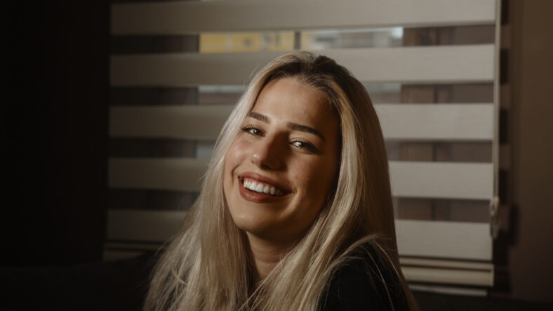 Young blonde charming attractive pretty blonde hair woman looking at camera in office or at home, dressed in blond black
