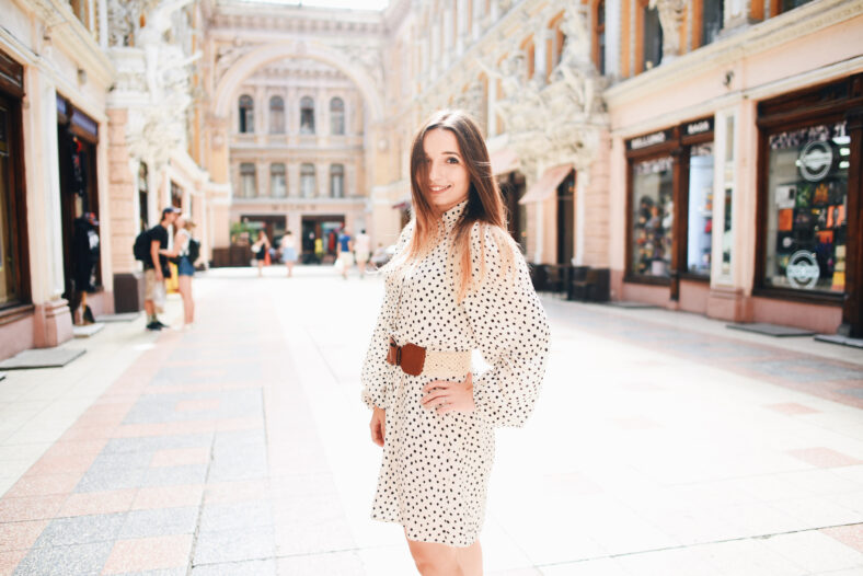 Girl in a white dress with polka dots on the background of the city. Urban lifestyle.