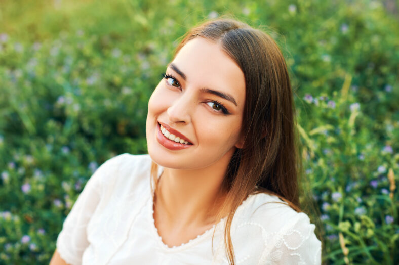 Fashion portrait of young woman resting on fresh green grass, wearing white dress