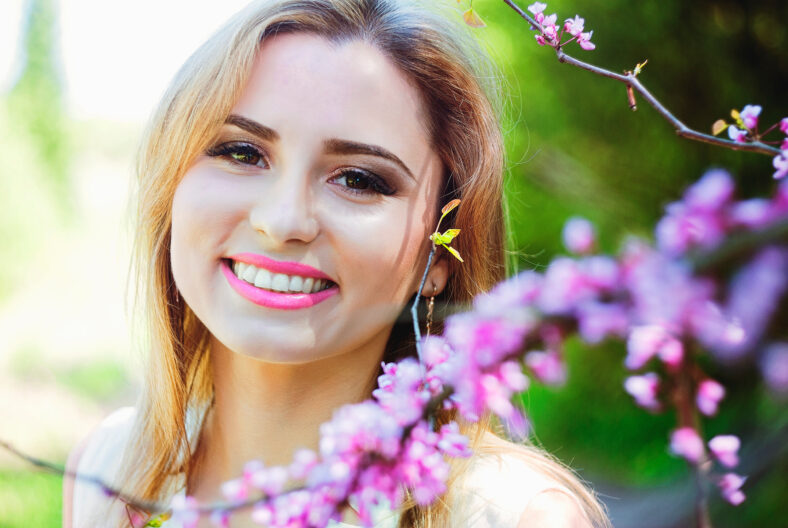 Portrait of young attractive woman in spring garden with blooming pink flowers. Spring background. Woman's Day. Greeting card.