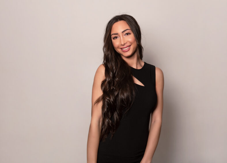 Beautiful young woman with long shiny black hair and natural make-up posing in dress on grey background