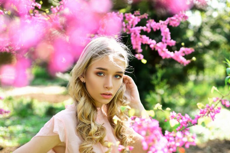 Young woman enjoy flowers in garden. Girl walks in park on sunny spring day