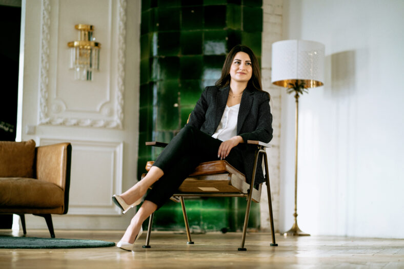 Sitting on a chair. Modern and stylish office. Illuminated by sunlight. Hardwood floors and a Vintage chair. Calm mood. The manager is a female student in a business suit of European appearance.