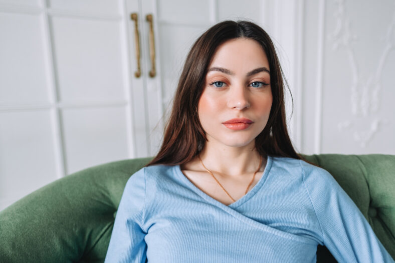 Portrait of attractive pretty young woman in casual clothing sitting on a sofa and looking on camera.