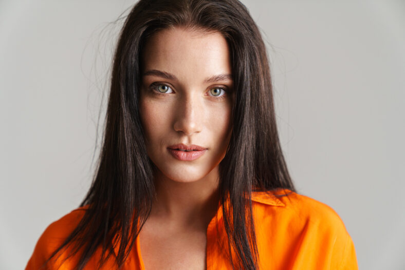 Young brunette woman wearing shirt posing and looking at camera isolated over grey background