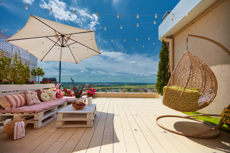 a cozy rooftop patio with wooden pallet furniture and hanging swing chair at sunny summer day