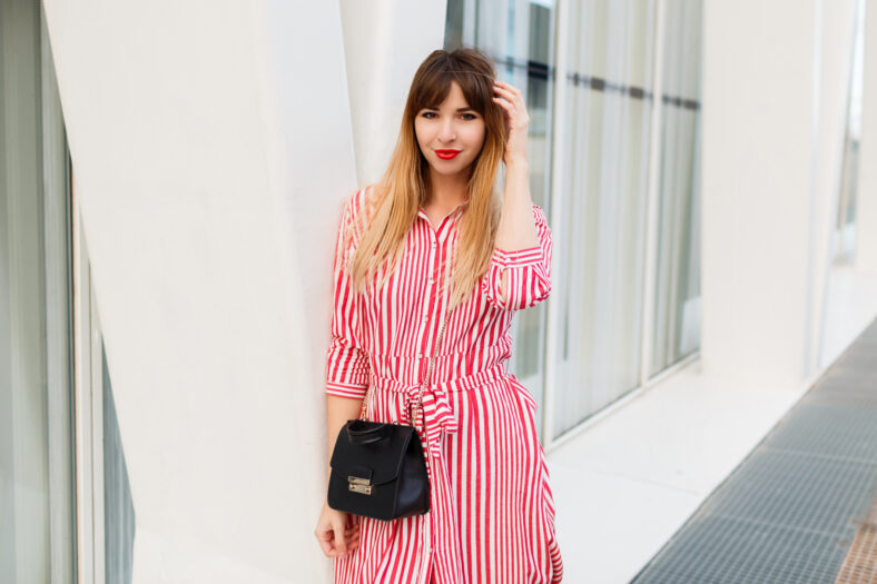 Fashion photo of pretty woman in red dress posing on the street.