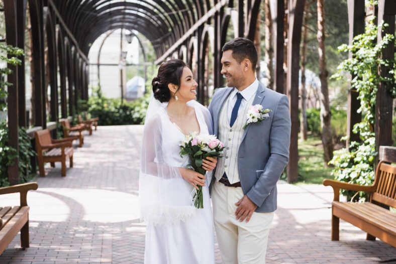 Side view of newlyweds smiling at each other in park