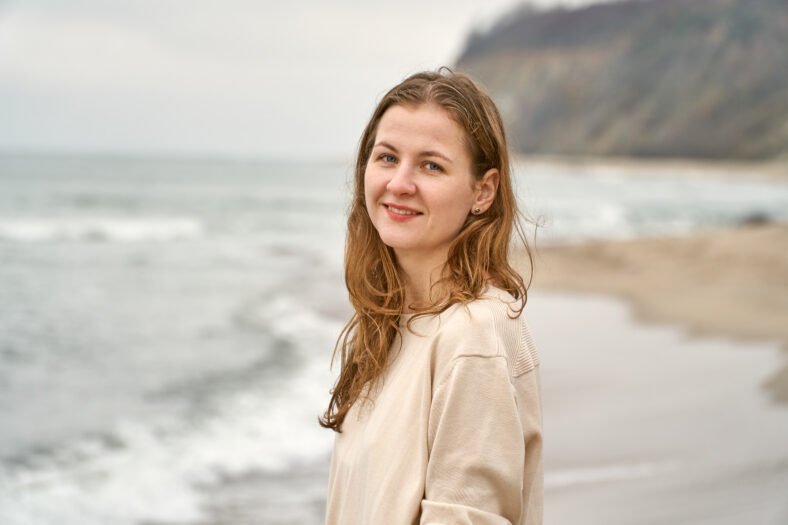 Girl on the beach have fun. Caucasian beautiful woman is happy on the beach against the background of the sea. Beige clothes and sand in the fall. High quality photo