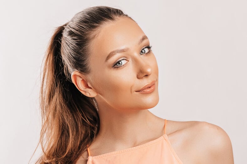 Hermosa joven sonriendo y posando mirando la cámara sobre un fondo blanco aislado. Mujer morena positiva. Mirada amable. Cara de belleza.