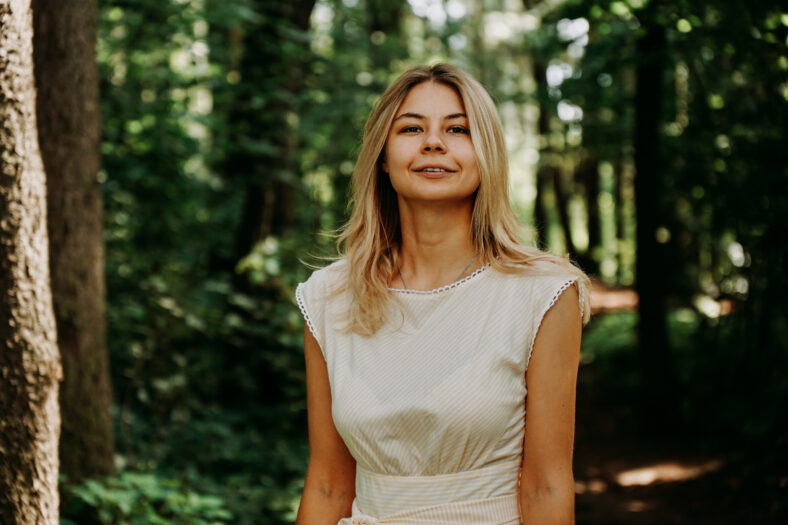 Attractive young woman enjoying her time outside in park. Young blonde in a white dress in a green park. Woman on the background of summer trees
