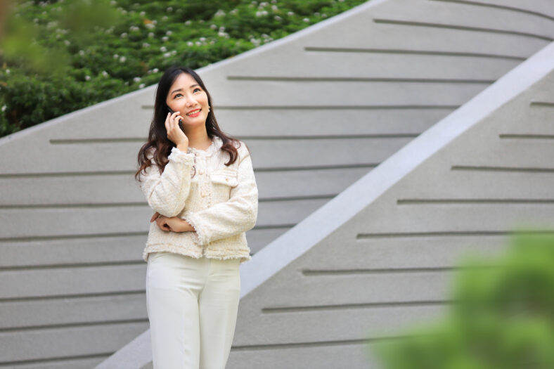 Asian lady using mobile phone while walking along the modern building in urban downtown area for communication and technology concept