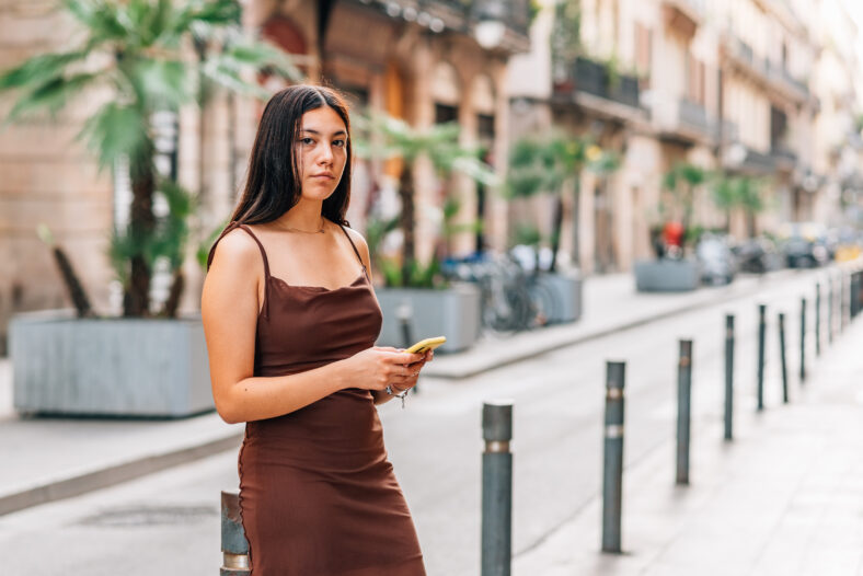 horizontal portrait of a young chinese woman using her phone in the streets and looking at camera