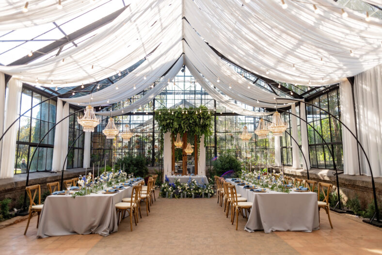 Wedding banquet hall in the greenhouse, tables are set, decorated with fresh flowers, candles, crystal chandeliers. Soft selective focus.