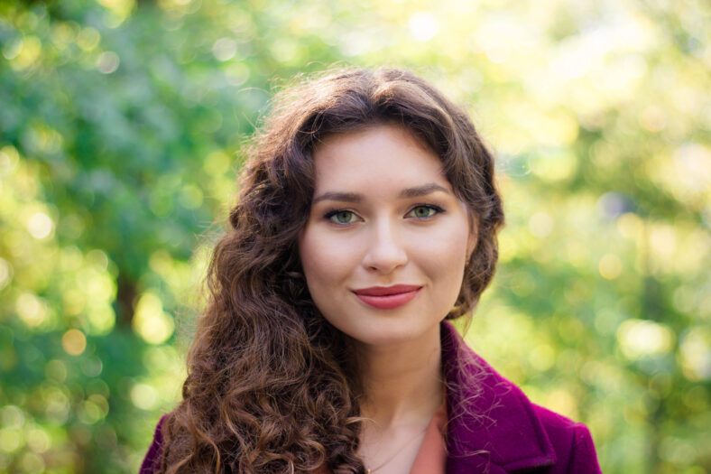 Hermosa mujer en Autumn Park. Cara de primer plano. Cabello rizado. La joven sonríe.