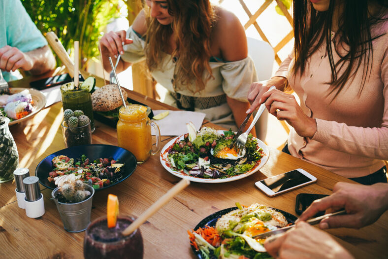 Young friends having fun eating brunch at healthy food restaurant - Focus on right girl hand