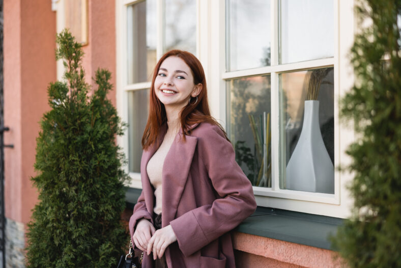 young cheerful woman with red hair standing near building,stock image