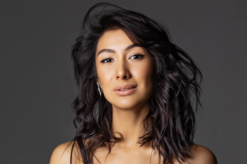Beauty face with nude makeup. Smiling asian woman with wavy long black hair close up on gray background