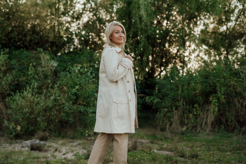 A beautiful adult woman with blond hair and a light raincoat smiles