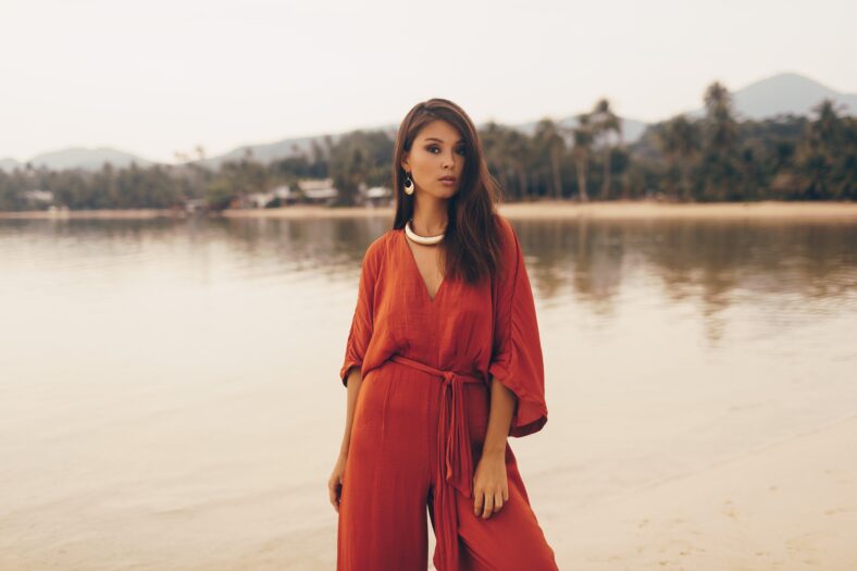 Asian woman in seductive red dress posing on the beach. Golden jewelry. Tropical island.