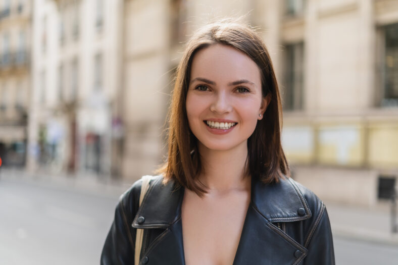 Retrato de mujer joven feliz en chaqueta de cuero sonriendo mientras mira a Camera en Francia, Stock Image