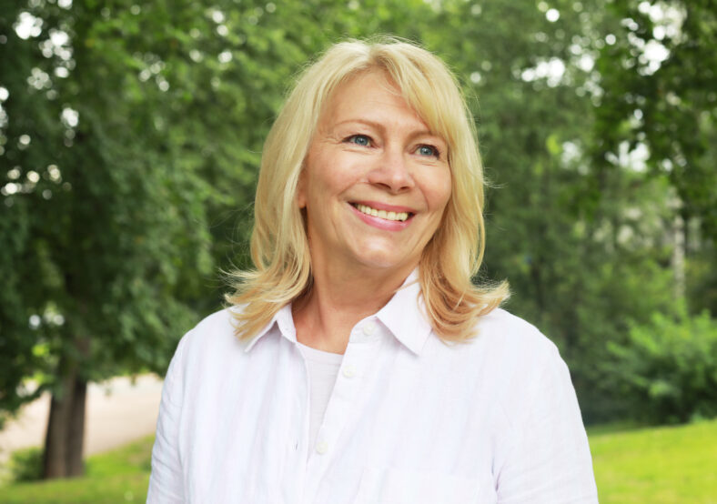 Beautiful blonde woman of sixty years old in a summer park, close-up portrait. The lady smiles and feels happy. Gold age.
