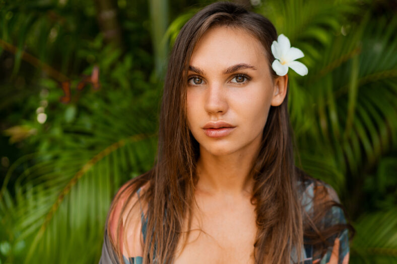 Close Graceful Woman model with plumeria flower in hairs posing in tropical nature.
