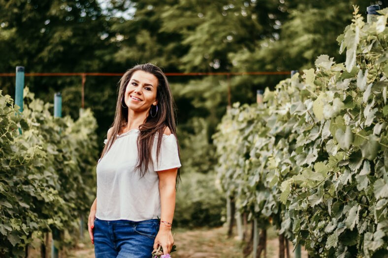 Stylish boho woman walking with wildflowers in hand in sunset light. Atmospheric moment. Summer travel. Young female in Rustic linen cloth relaxing in summer meadow near a Wineyard