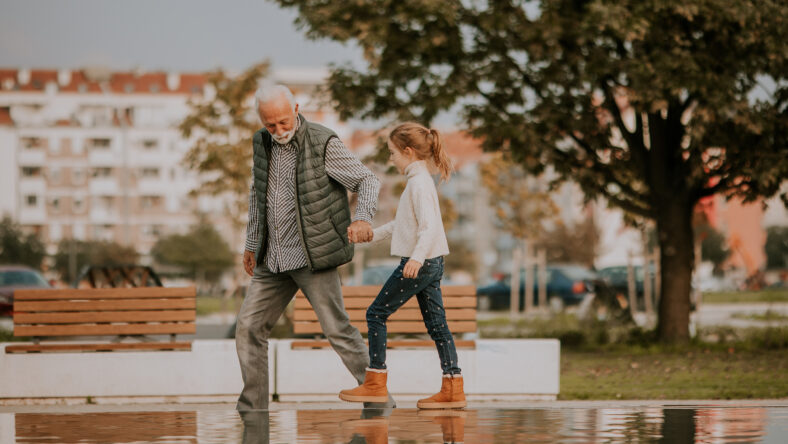 Handsome grandfather spending time with his granddaughter by small water pool in park on autumn day