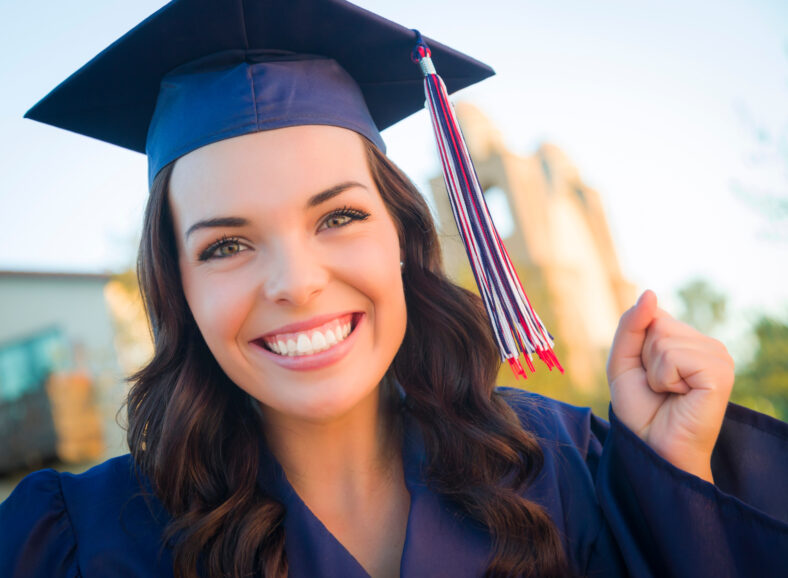 Happy Graduating Mixed Race Woman In Cap and Gown Celebrating on Campus.