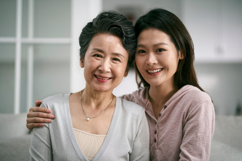 portrait of asian elderly mother and adult daughter sitting on couch at home happy and smiling