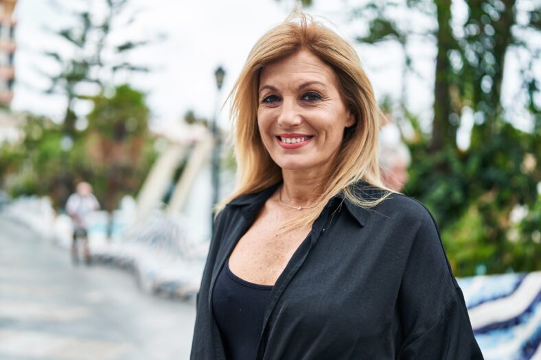 Mujer rubia de mediana edad sonriendo segura de pie en la calle