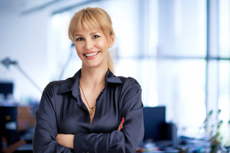 Happy business woman with blond hair standing at the office with folded arms.
