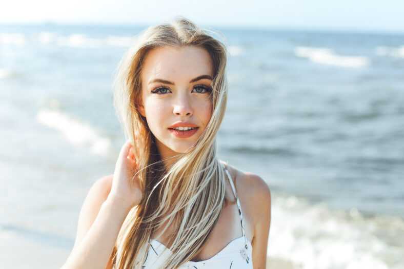 Happy blonde woman in free happiness bliss on ocean beach standing straight and posing.