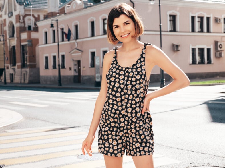 Young beautiful smiling hipster woman in trendy summer overalls clothes. Sexy carefree model posing on the street background at sunset. Positive brunette female. Cheerful and happy